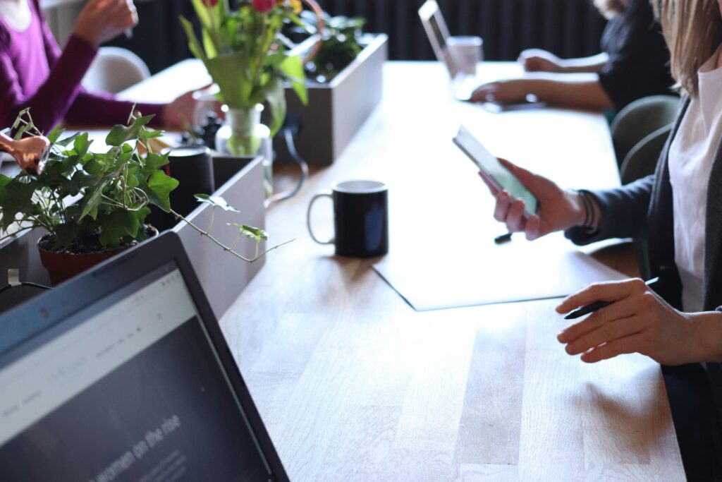 Contemporary office environment featuring teamwork with laptops, coffee, and greenery.